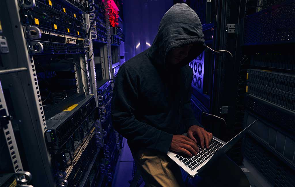 Focused Hacker Typing on Laptop in Server Room
